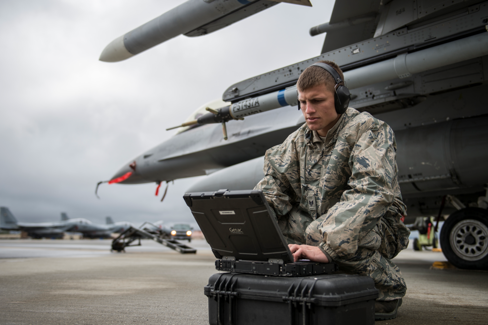 Military Personnel operating computer next to military aircraft